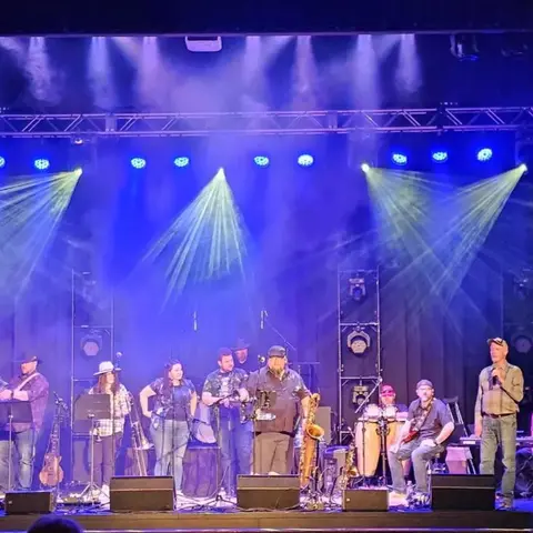 A band performs on a stage with blue lighting and stage lights.