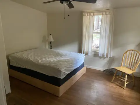 An interior shot of a bedroom with a bed, a chair, and a window.
