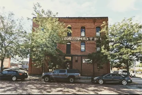 An exterior view of an old brick hotel building with parked cars in front.