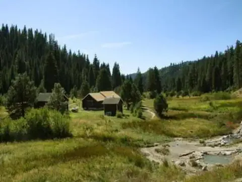 A scenic view of a valley with cabins surrounded by pine trees and grassy fields.