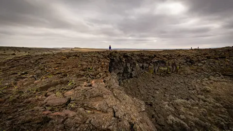 A wide landscape showing dark volcanic rock formations under a cloudy sky.