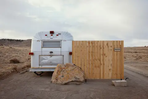 A vintage trailer parked next to a wooden fence in a desert landscape.