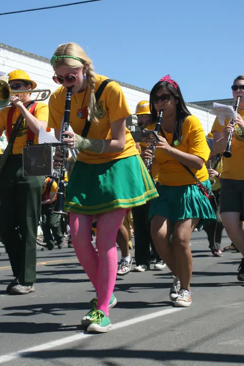 A marching band plays instruments while walking down a street.