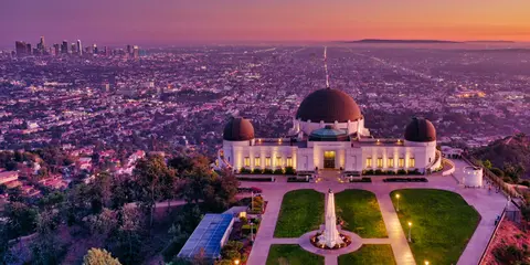 An observatory building stands on a hill overlooking a sprawling city at sunset.