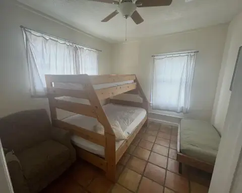 A bedroom furnished with a wooden bunk bed, a single bed, and an armchair.