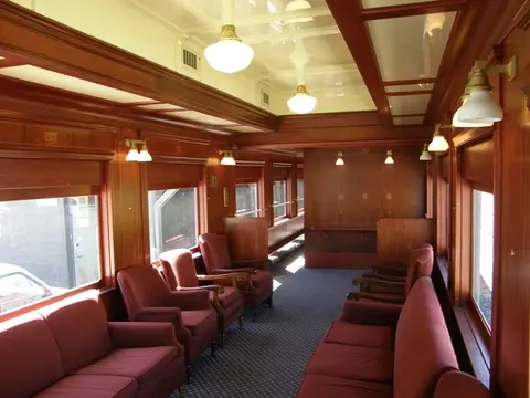 An interior view of a vintage train car with wood paneling and red seating.