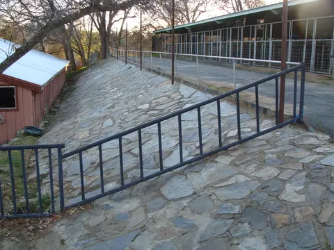An outdoor paved path with a stone retaining wall and metal railings.