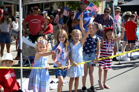 Children holding American flags behind a yellow caution tape at an outdoor event.
