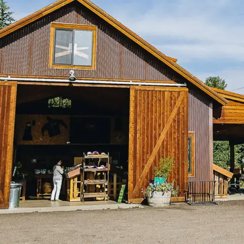 A rustic metal barn with wooden sliding doors and an open entrance showing its interior.