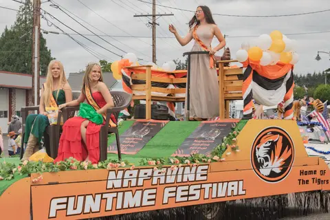 Three young women ride on a decorated festival float in a parade.