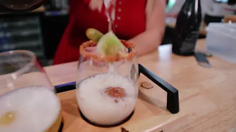 A drink is poured into a garnished glass set in a wooden flight.