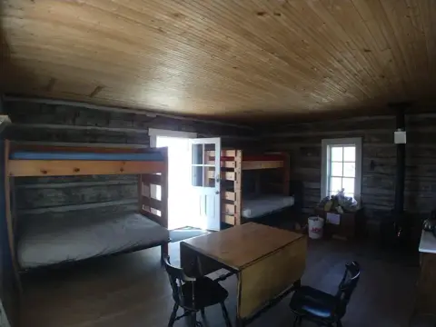 Interior of a rustic cabin with bunk beds, a table, and chairs.