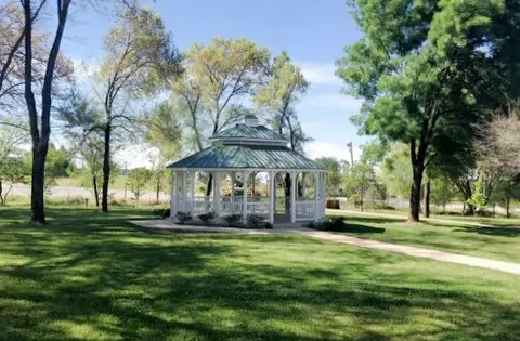 A white gazebo stands in a grassy park surrounded by trees.