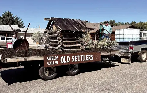A parade float carrying a miniature log cabin replica.