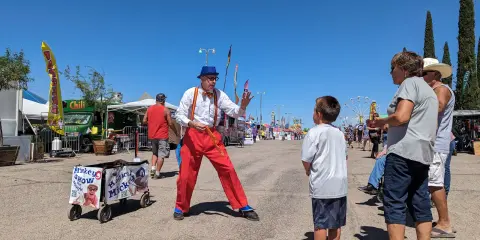 A street performer in a clown costume entertains a boy at an outdoor fair or festival.