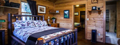 A rustic bedroom inside a log cabin with a log bed and cowboy-themed bedding.