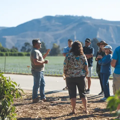 A guide speaks to a small group of people outdoors near fields and mountains.