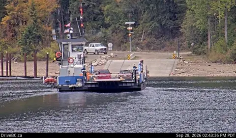 A ferry carrying vehicles on a body of water near a boat ramp.