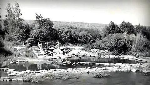 Black and white photo of a natural pool with a car parked nearby.