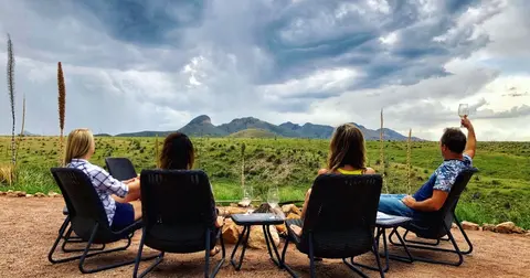 Four people sit in outdoor chairs enjoying a view of mountains and a cloudy sky.