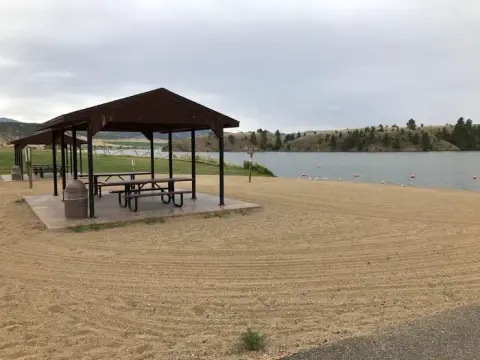 A picnic shelter sits on a sandy beach by a body of water.