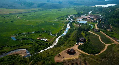 An aerial view of a winding river flowing through a lush green valley with buildings and roads.