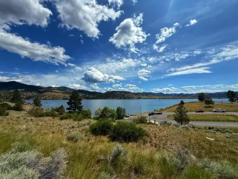 A scenic landscape view of a large body of water surrounded by grassy hills and mountains under a partly cloudy blue sky.