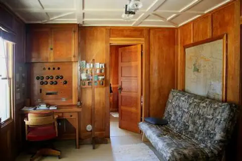 A wood-paneled room features a desk, a sofa, and an open doorway.