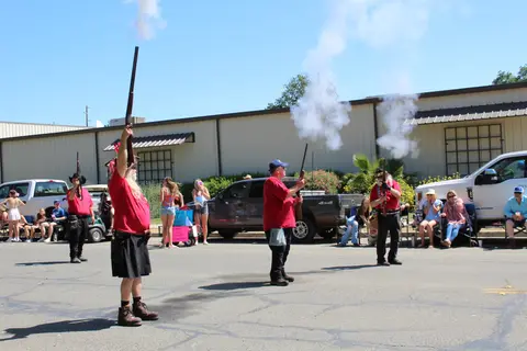 People firing muskets outdoors in a street.