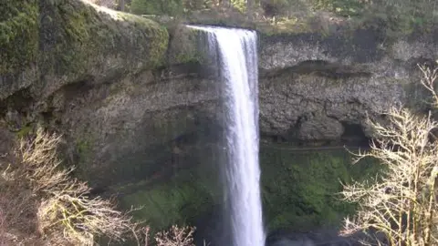 A tall waterfall drops over a cliff into a rocky canyon.
