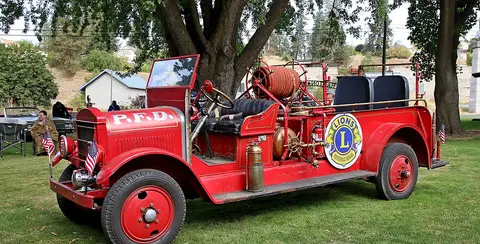 A vintage red fire truck parked on grass outdoors.