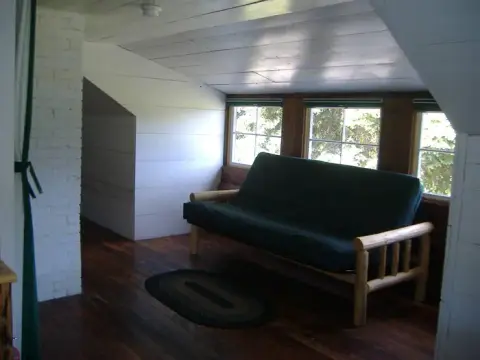 An attic room with a wooden futon and windows overlooking greenery.