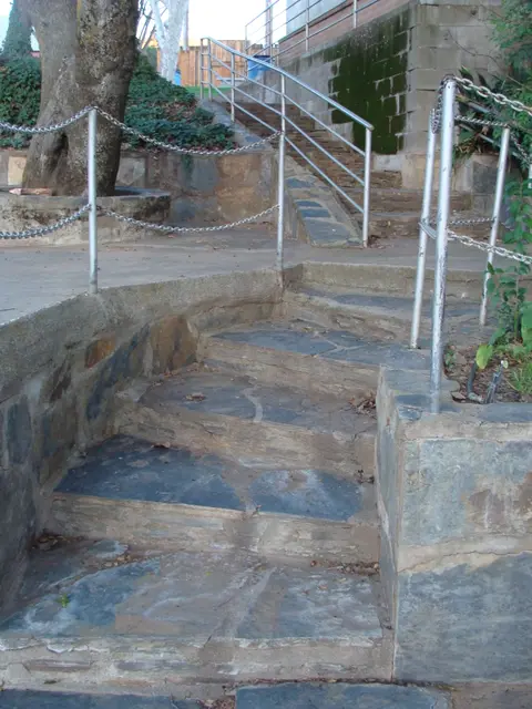 Stone outdoor steps lead upward past retaining walls and metal railings.