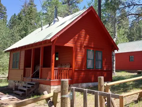 A red wooden cabin with a porch stands in a forest.