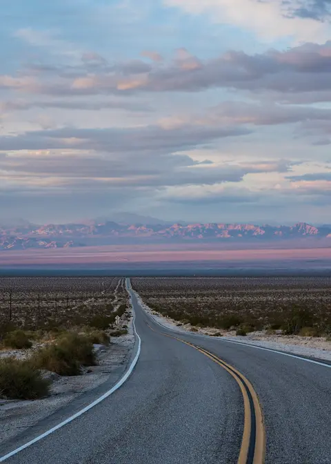 A long desert highway winds through an arid landscape under a cloudy sky.