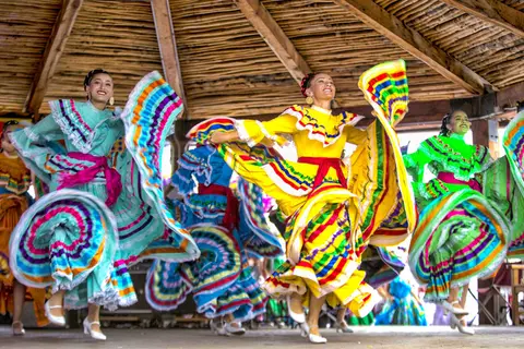 Dancers in colorful traditional dresses perform under a wooden structure.