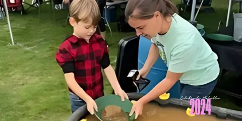 A child and an adult pan for gold at an outdoor event.