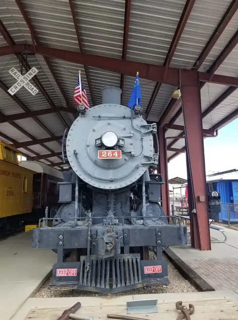 A front view of a grey steam locomotive parked under a pavilion.