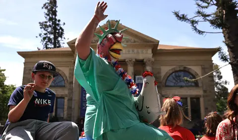 A person dressed as the Statue of Liberty with a chicken mask waves during an event.