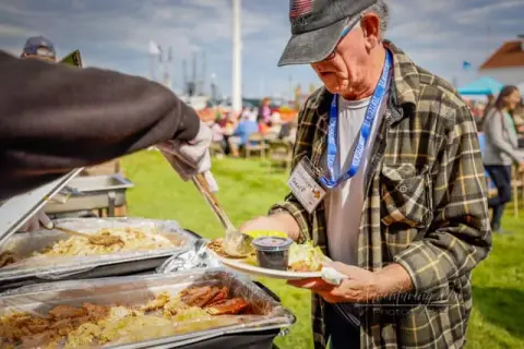 A man being served food from buffet trays at an outdoor event.