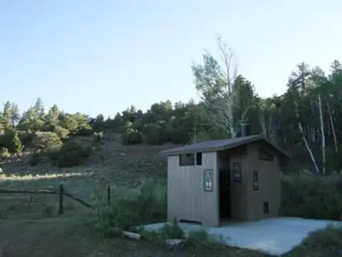 An outdoor restroom building stands near a wooded hillside.