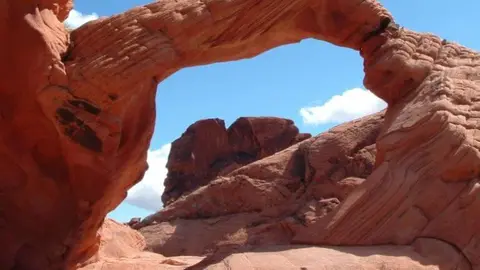 A natural red rock arch framing a cloudy blue sky and desert landscape.