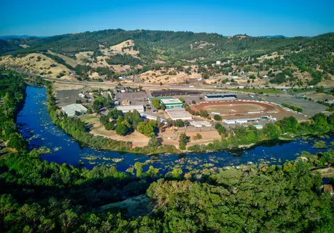 An aerial view shows a racetrack and buildings nestled in a bend of a river surrounded by hills.