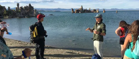 A guide speaks to a group of people by a lake with tufa towers.