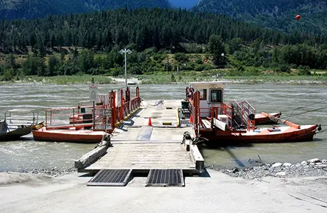 A cable ferry docked at a riverbank against a background of forested hills.