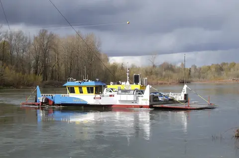 A car ferry crossing a river under a cloudy sky.