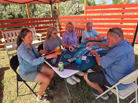People playing cards at an outdoor table under a tent.