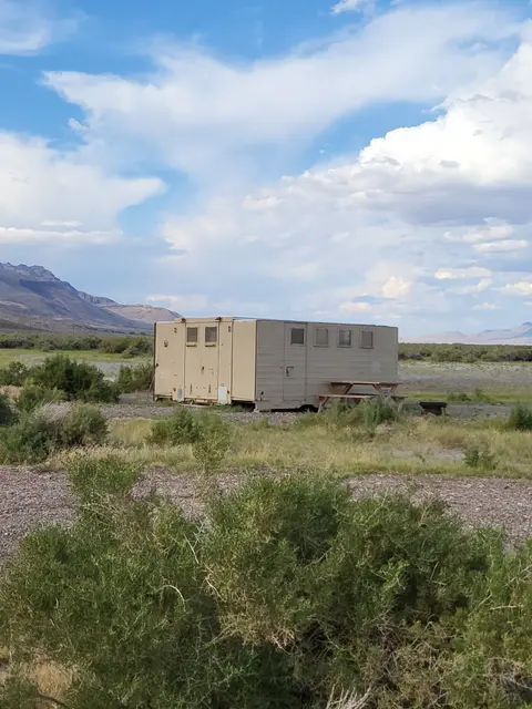A tan modular building stands in a desert landscape under a partly cloudy sky.