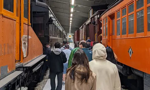A crowd of people walks between historic train cars inside a large building.
