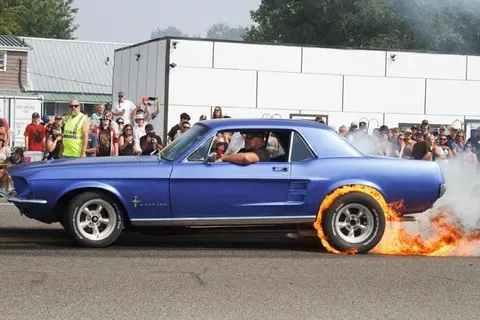 A blue car does a burnout with flames coming from its rear tire.